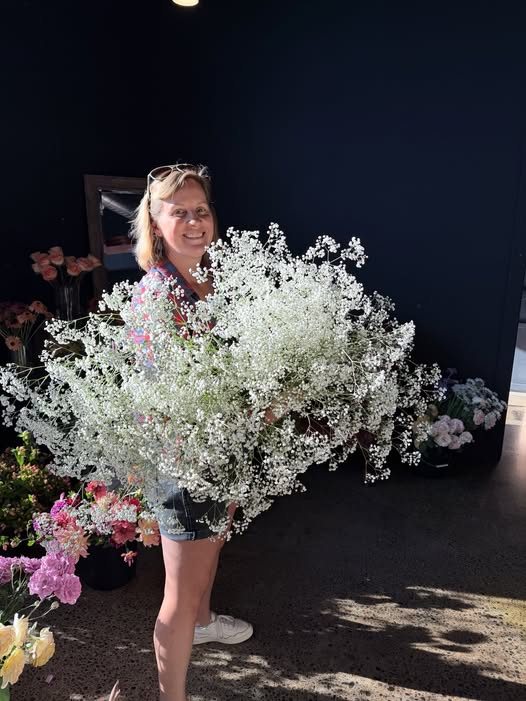 Woman holding a large bouquet of white baby's breath flowers, smiling, with dark background.