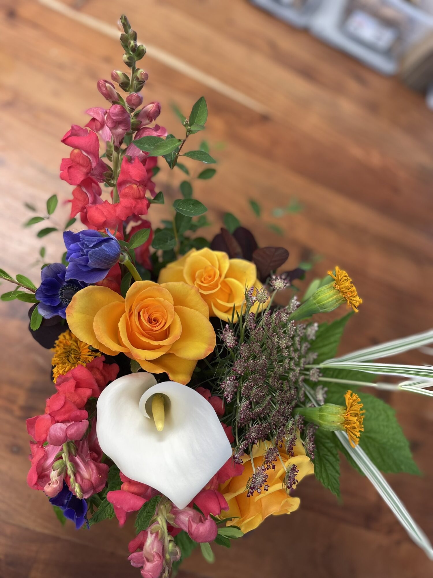 Colorful flower bouquet with roses, calla lily, and other flowers on a wooden surface.