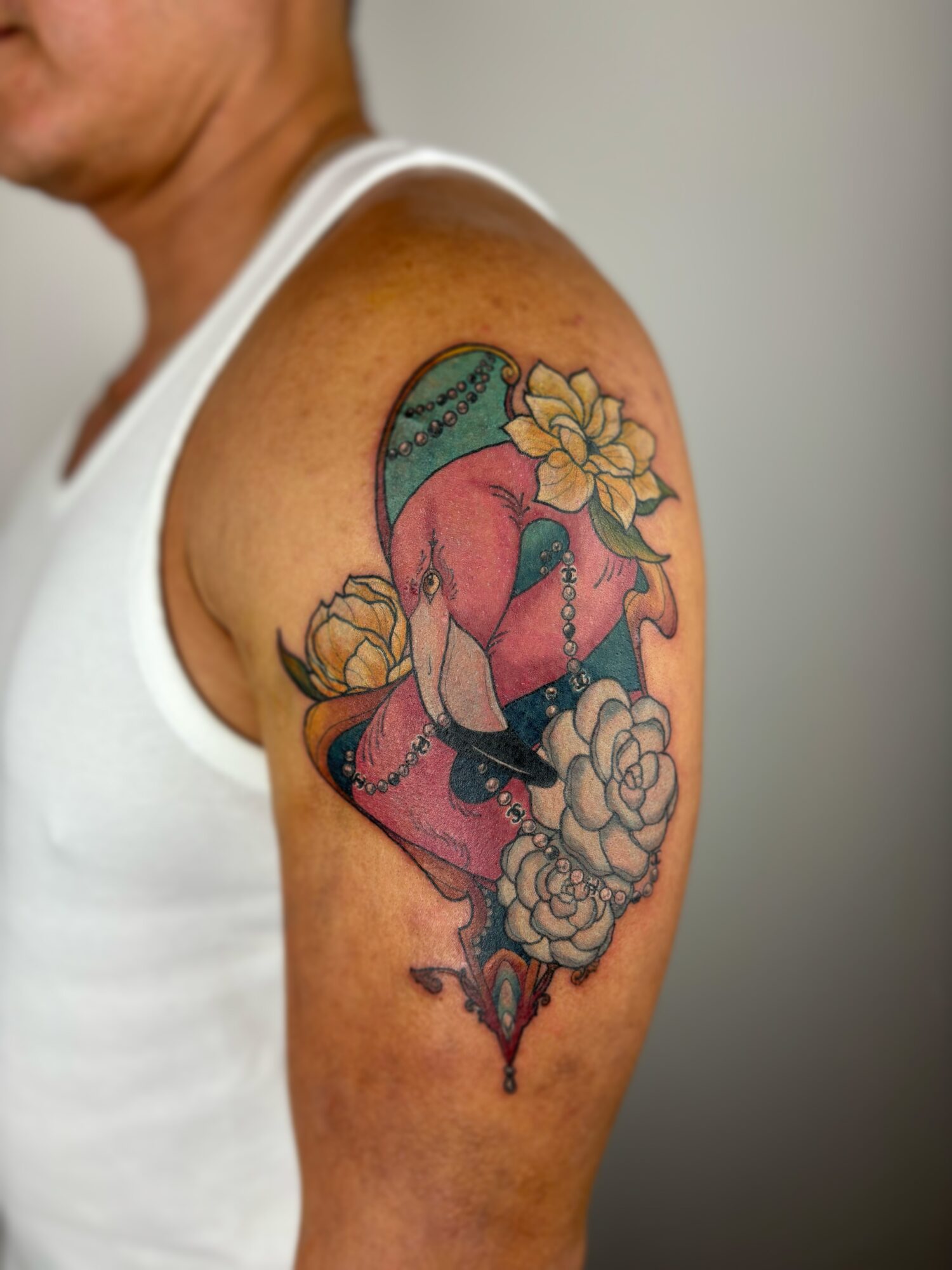 Colorful tattoo of a woman with a flower in her hair, surrounded by flowers on upper arm, on a person wearing a white tank top.