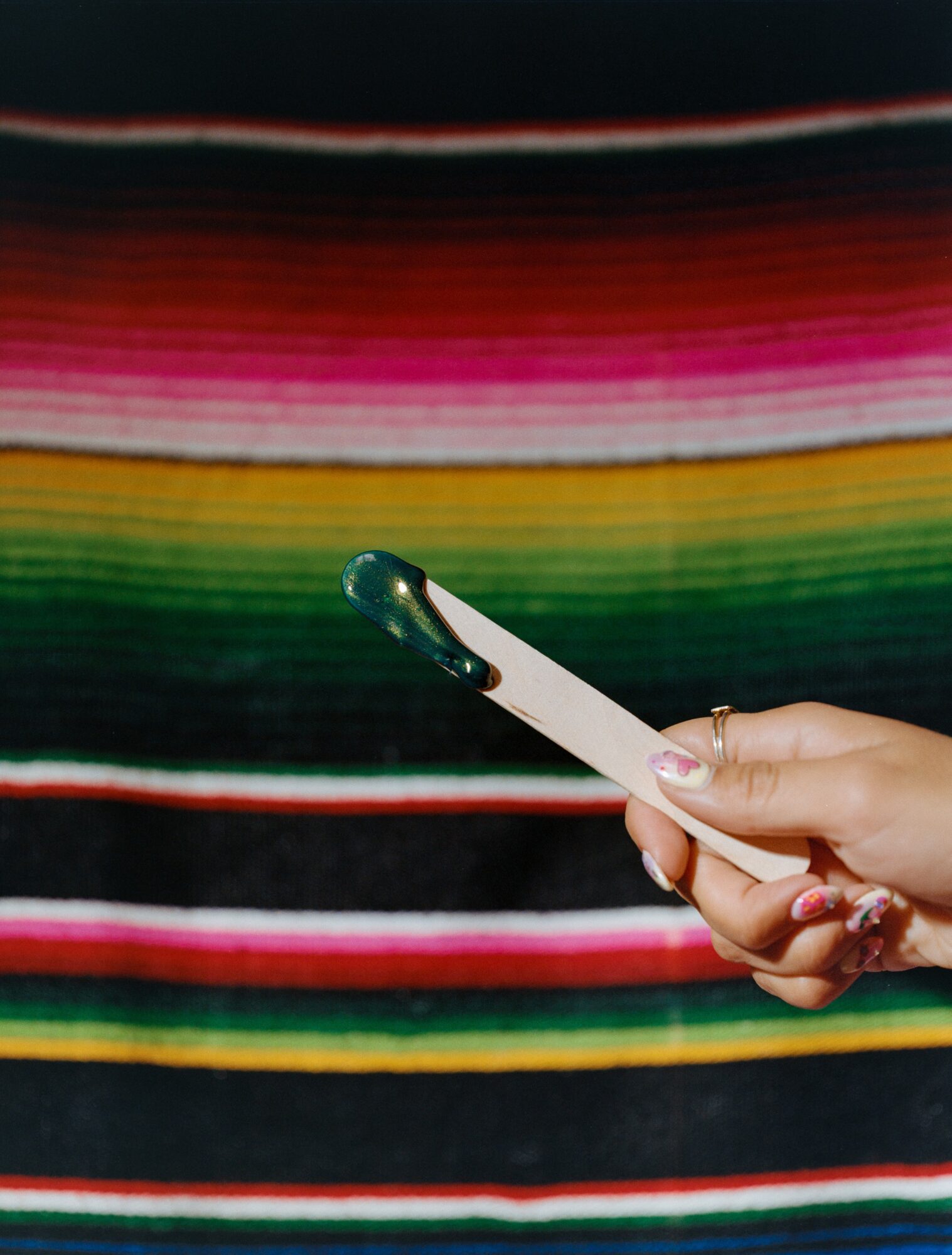 Person holding a pregnancy test in front of a colorful striped fabric background.