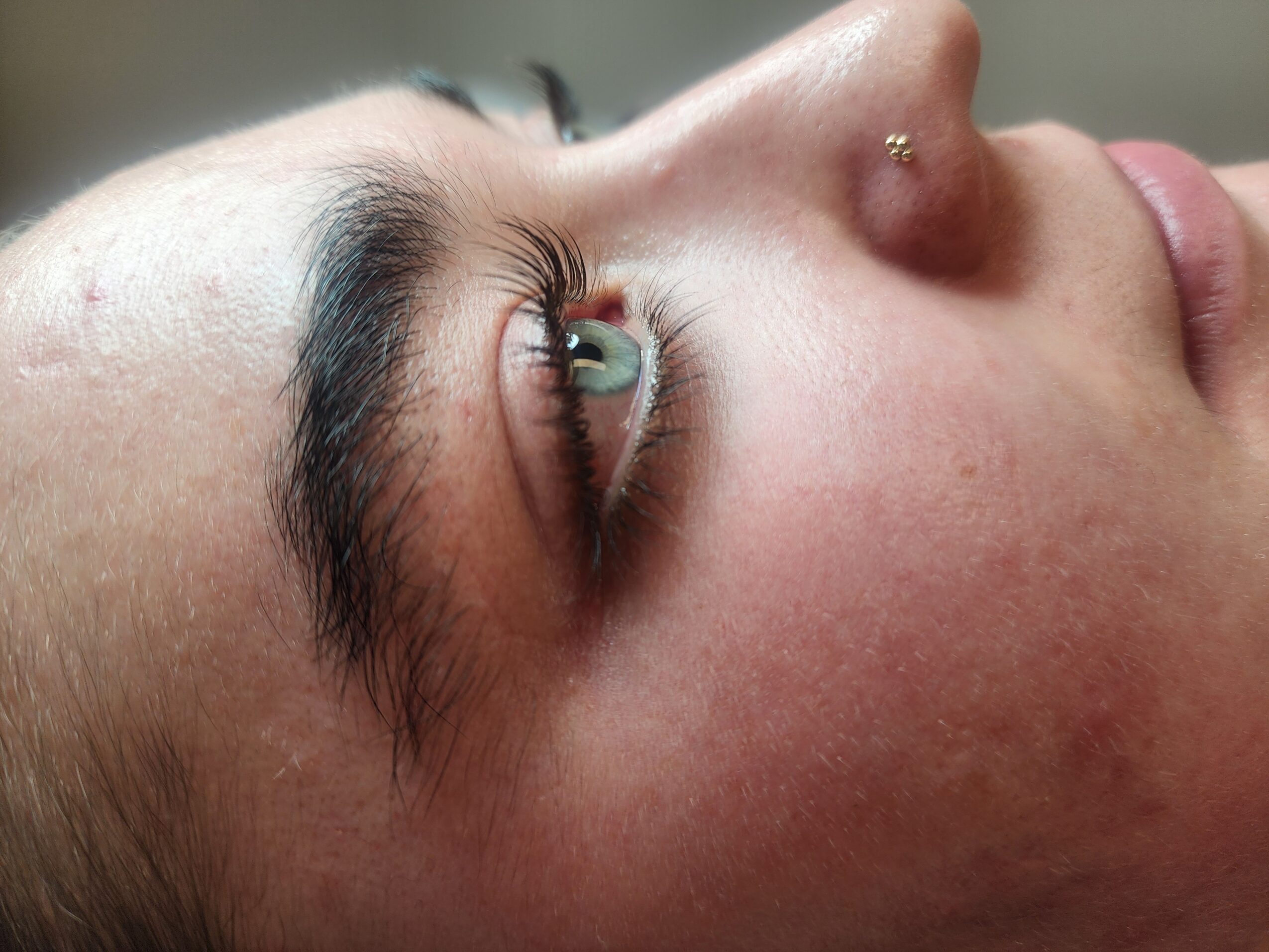 Close-up of a person's face showing eye, eyebrow, nose, and lips, with a nose piercing.