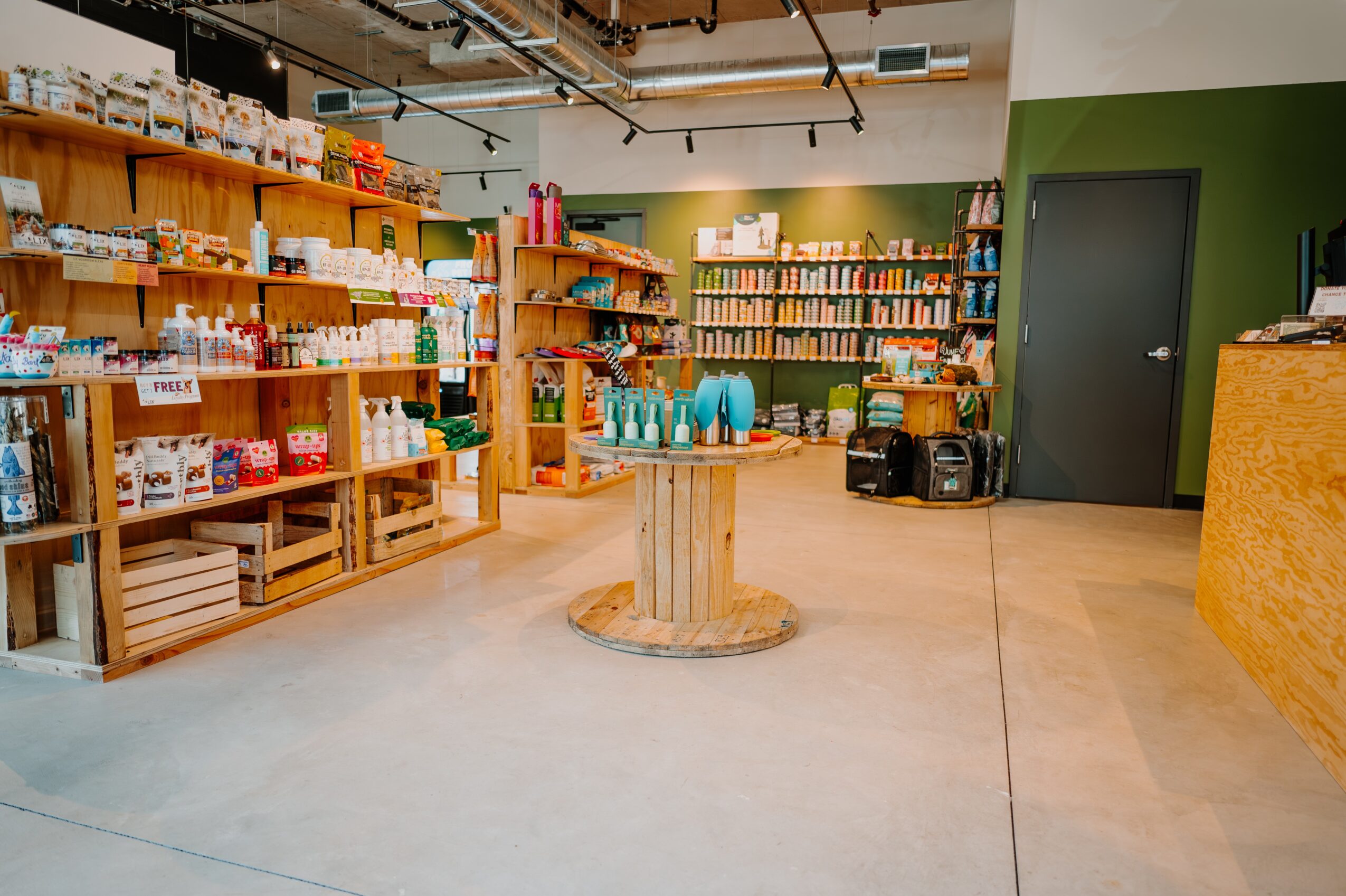Interior of a store with wooden shelves filled with various products, a central display table, and a green wall with a door.