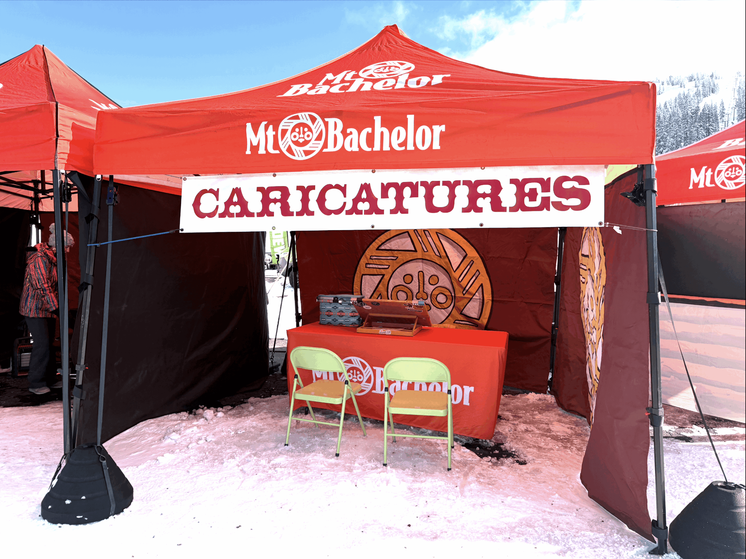 Red tent with 'Mt. Bachelor' and 'Caricatures' signs, two chairs, and a caricature drawing station inside, on pink ground.