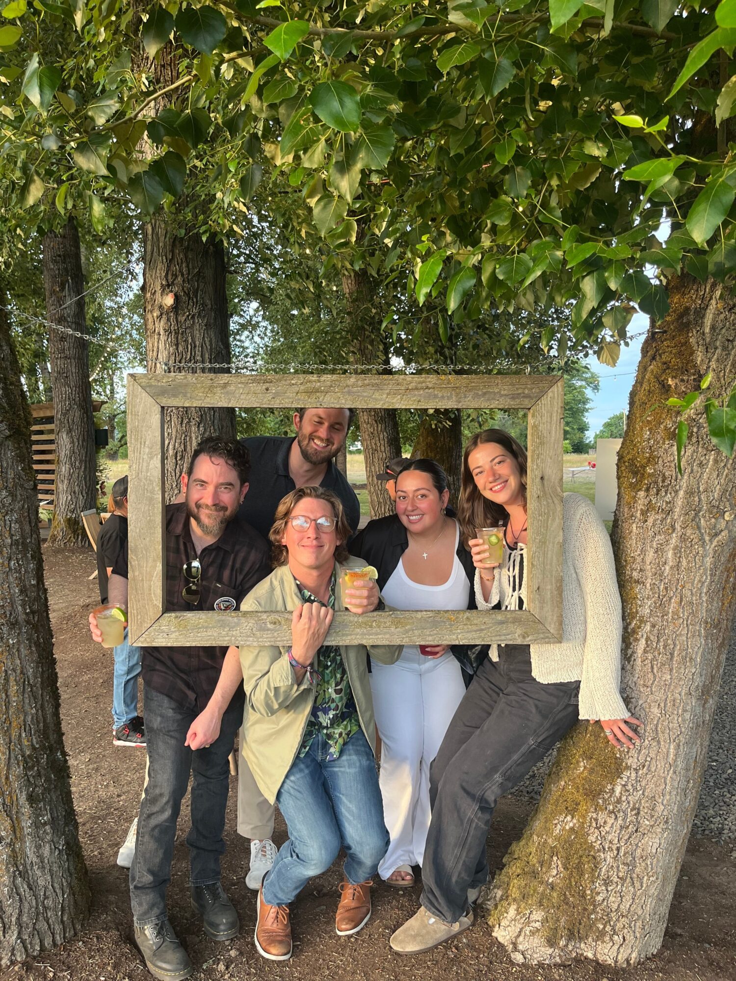 Four people standing behind a wooden frame outdoors, surrounded by trees and greenery.