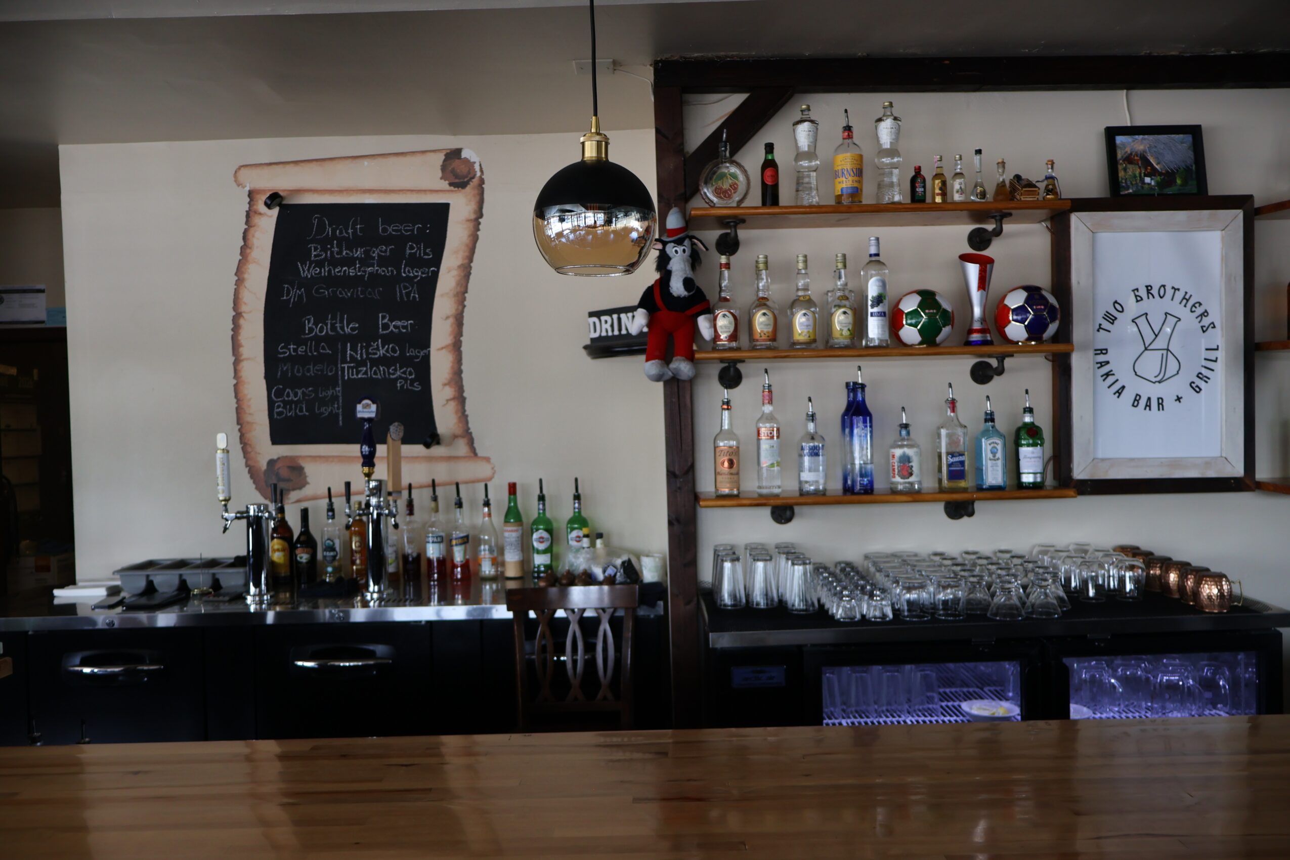 Bar area with bottles, glasses, and a chalkboard menu, shelves with bottles and decorations, and a hanging light fixture.