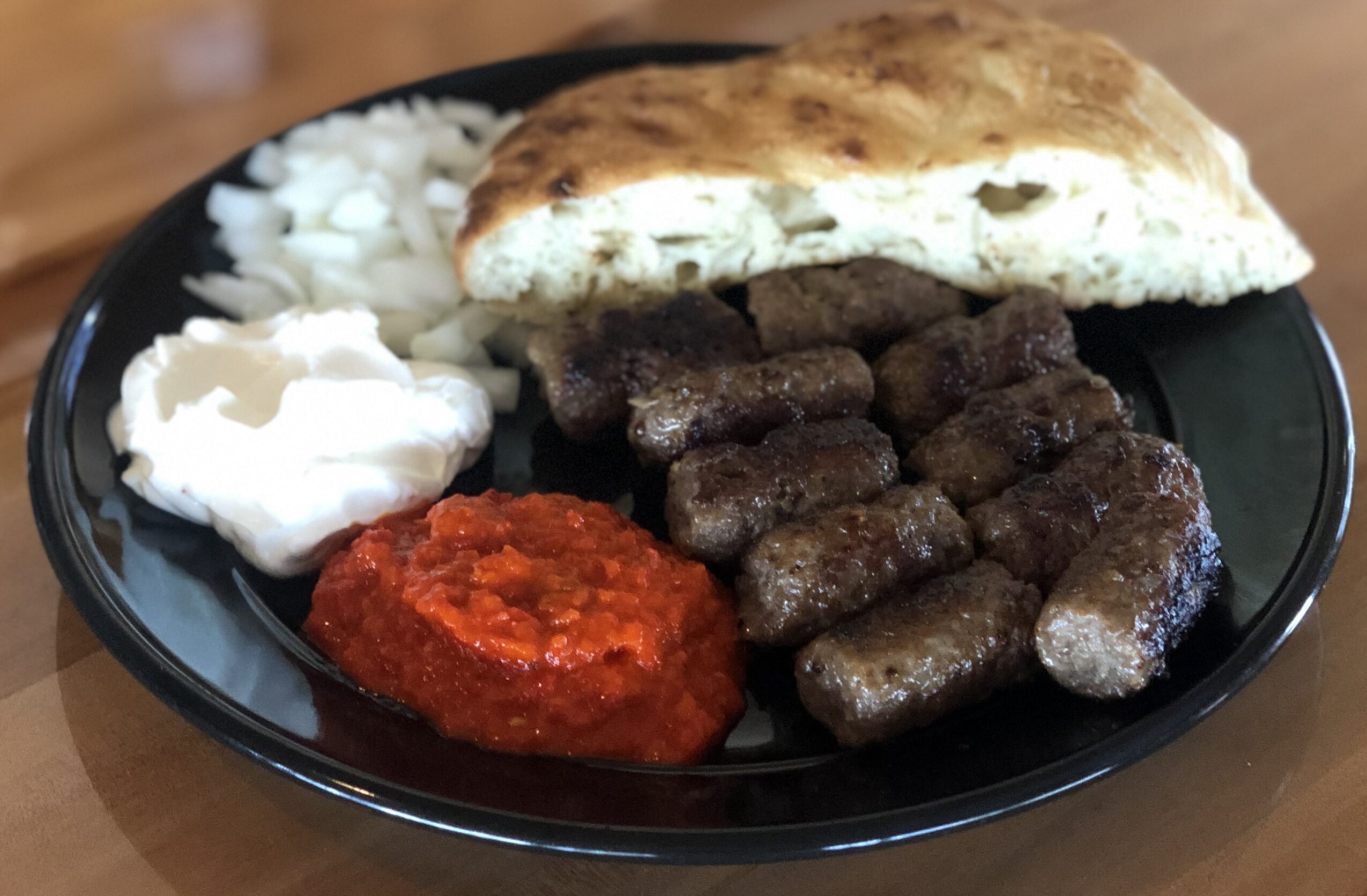 Plate with grilled meat, flatbread, white onions, red sauce, and a dollop of yogurt or sour cream.