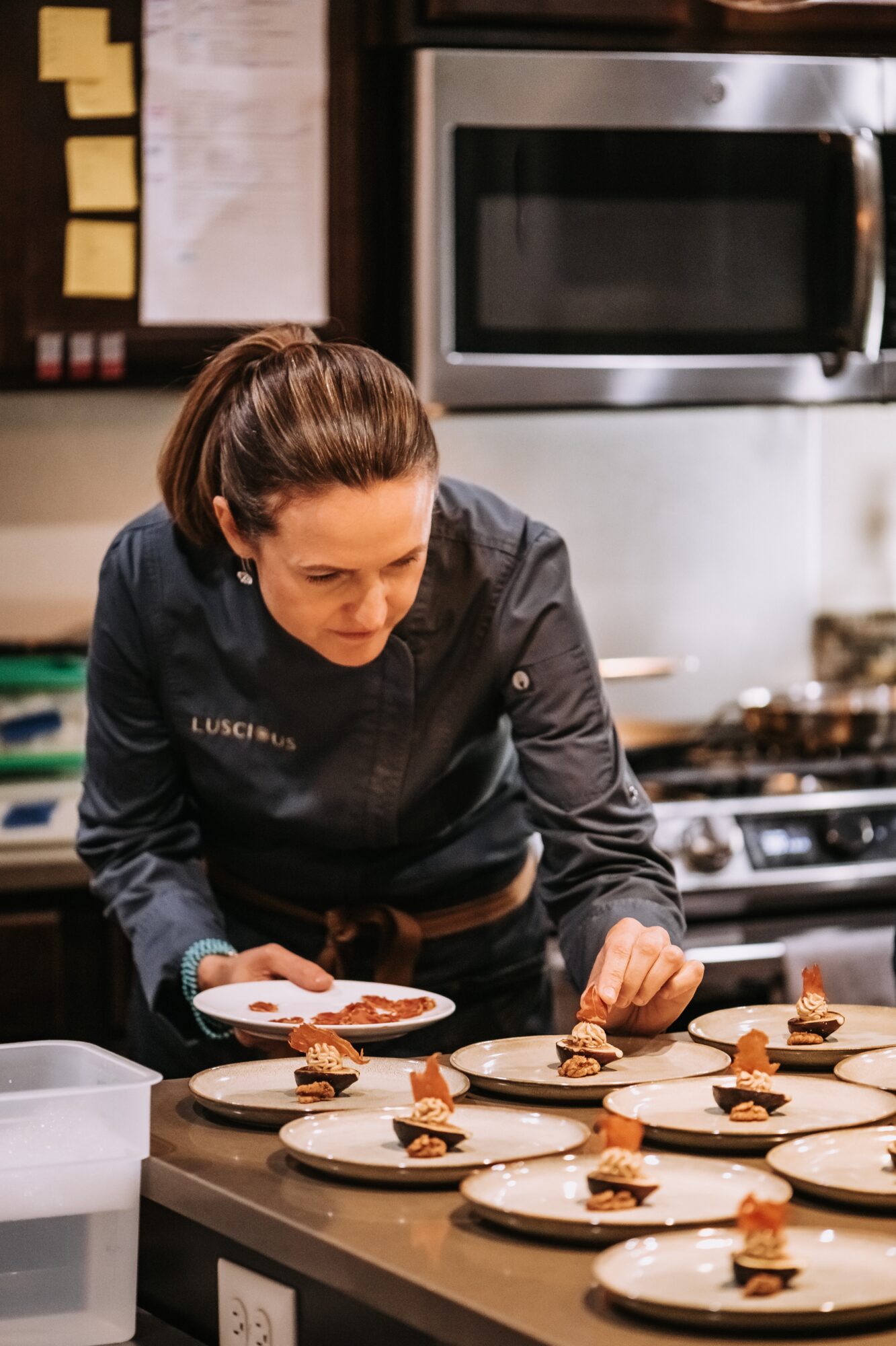 Woman in a kitchen preparing plates with food, focused on arranging dishes on a counter.