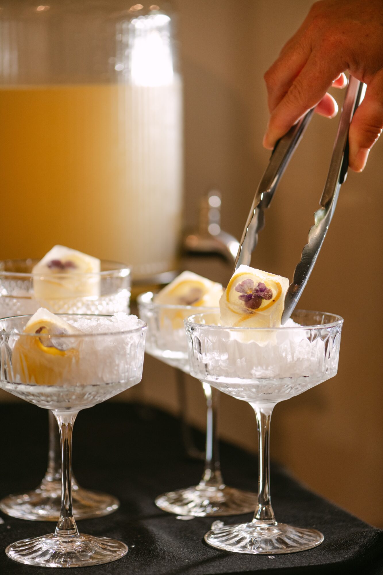 Person uses tongs to place dessert on a glass dish, with a large beverage in the background.