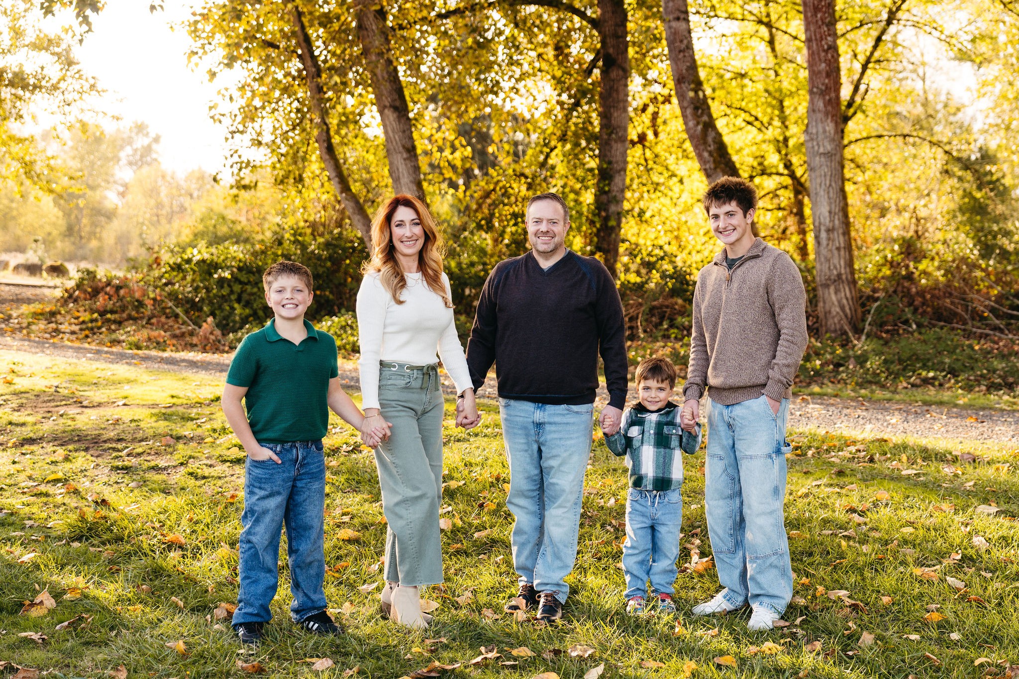 Family of five standing outdoors in a park with trees and sunlight, smiling at the camera.