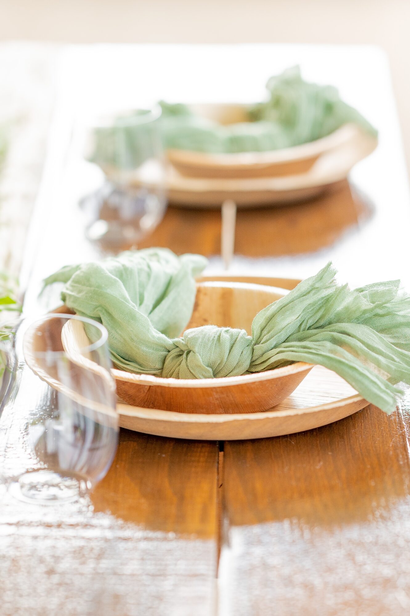 Wooden table with a bowl of leafy greens, a glass of water, and a mirror reflecting the scene, bright lighting.
