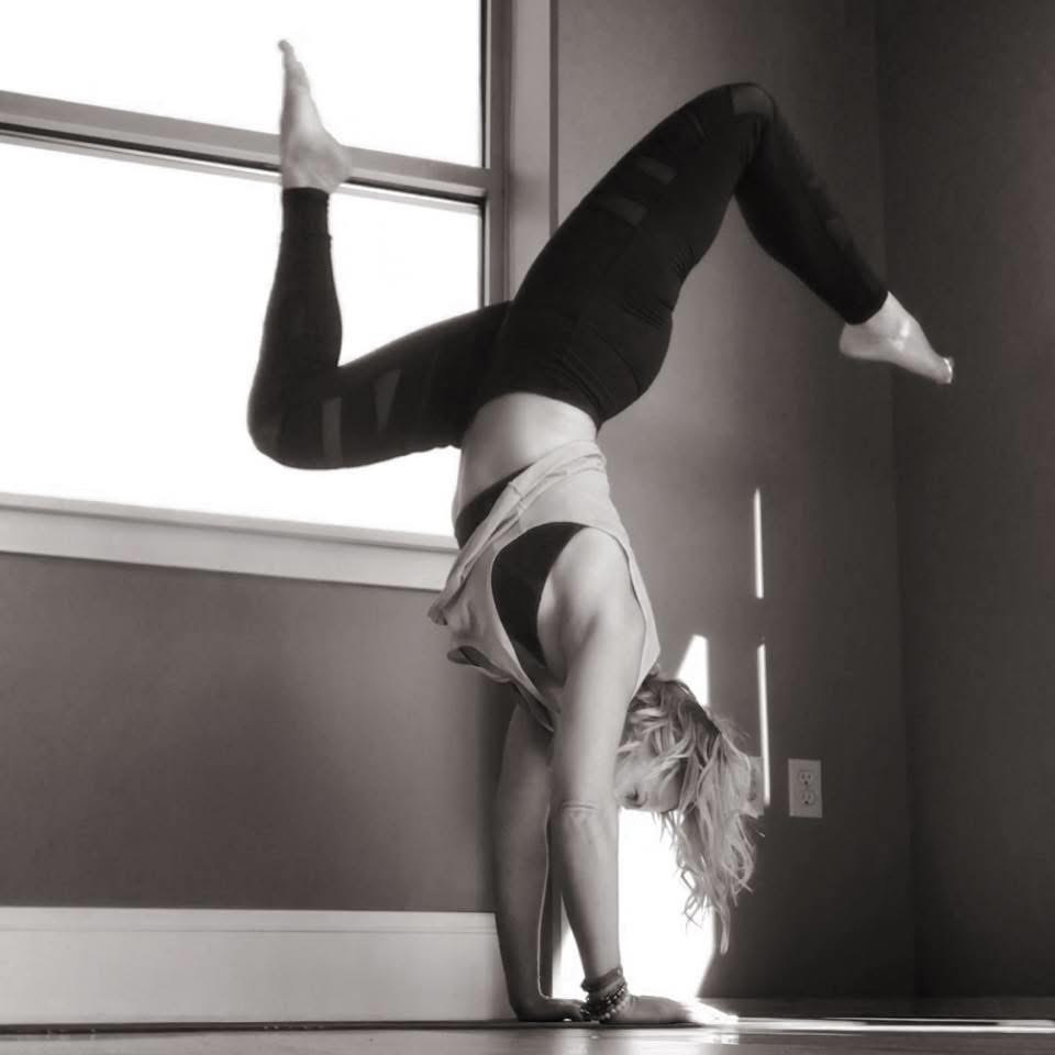 Person performing a handstand with one leg bent and the other extended, near a window in a room.