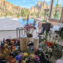 Indoor space with flowers, candles, and a view of mountains through large windows, bright and airy atmosphere.