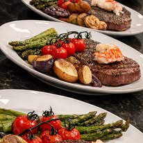 Plate with grilled steak, cherry tomatoes, asparagus, eggplant, and potato slices on a white dish.