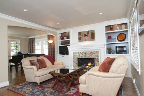Living room with two sofas, a fireplace, built-in shelves, and a colorful rug, with a dining area in the background.