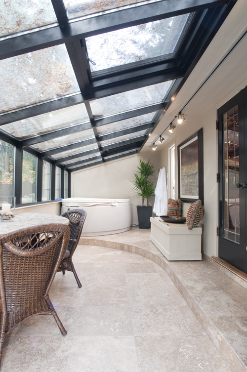 Indoor space with large glass ceiling, wicker chairs, a white bench, potted plant, and framed pictures on the wall.