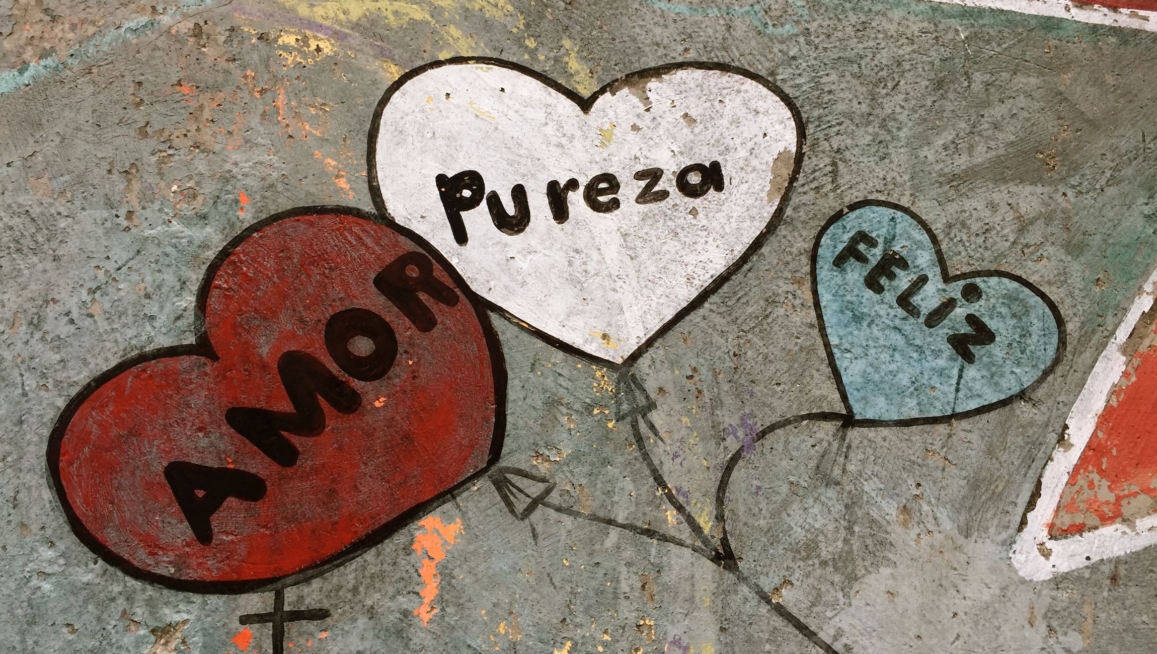 Three heart-shaped signs with words: 'Amor', 'Pureza', and 'Feliz', on a textured surface.