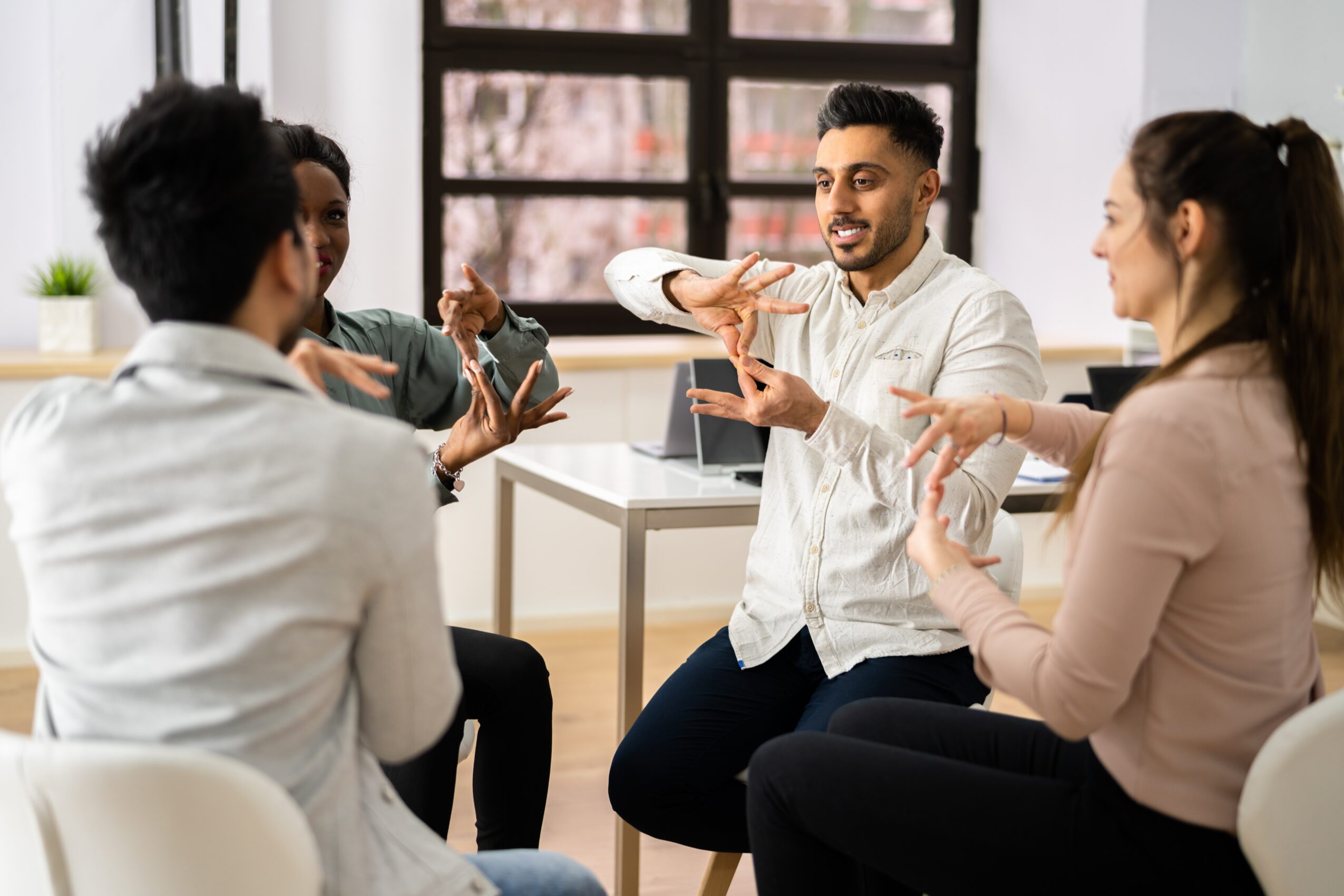 Group of five people sitting around a table, engaging in a discussion, with a man holding a shoe and smiling.