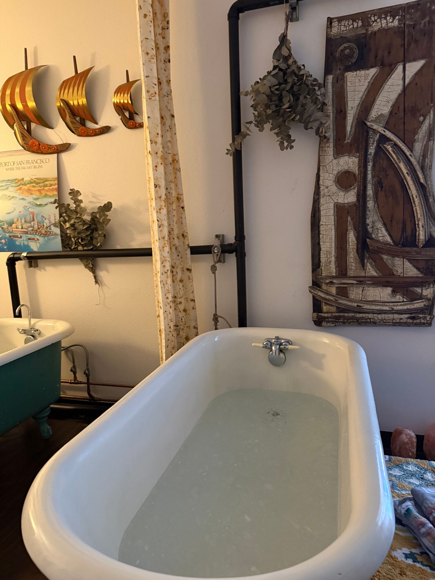 Bathtub filled with water, with a decorative wall hanging and plants in the background.