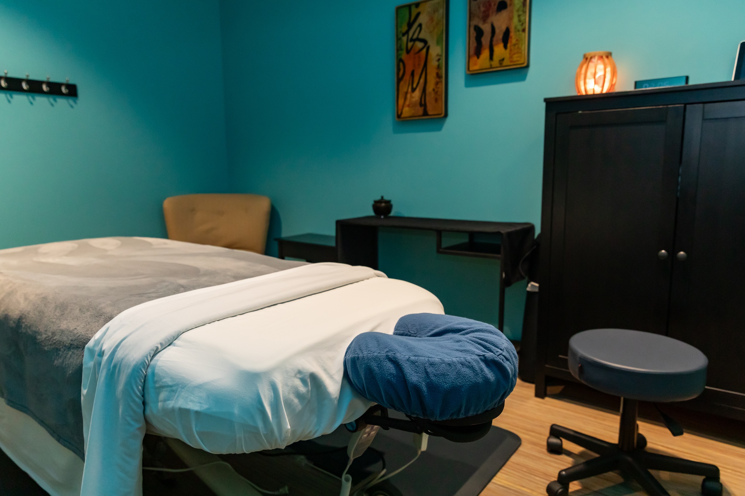 Bedroom with teal walls, bed with white and gray bedding, a chair, black cabinet, and wall art.