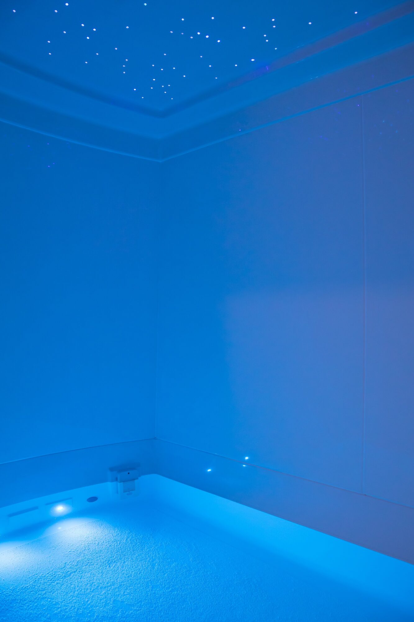 Ceiling with star-like lights and a blue-lit corner of a room, possibly a bathroom or spa area.