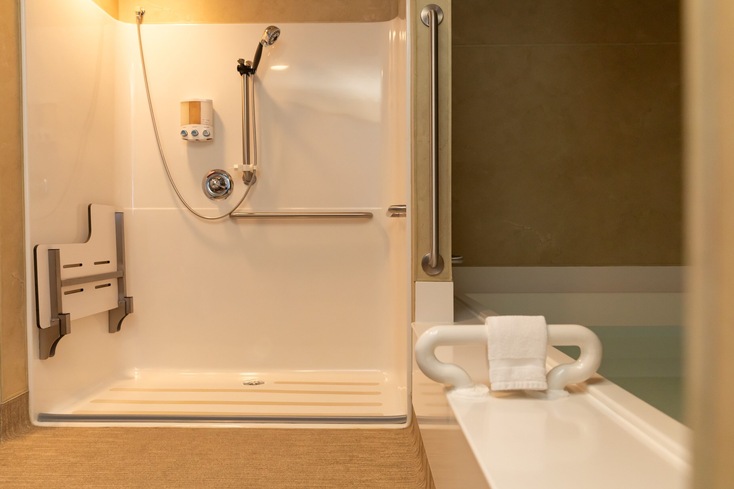 Shower stall with a grab bar, showerhead, and soap holder, next to a bathtub with a towel on the edge.