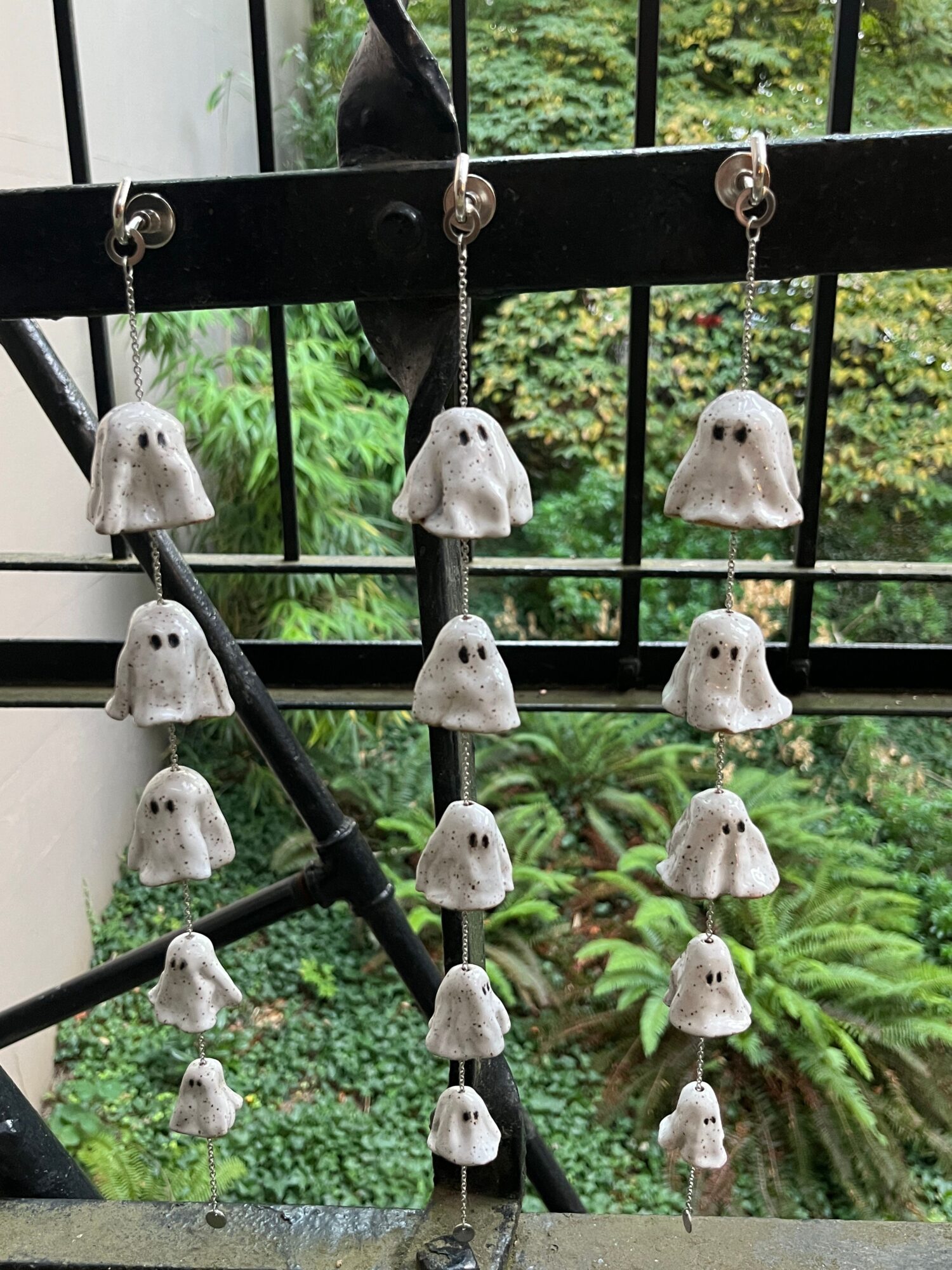 String of white ceramic bear-shaped beads hanging in front of a window with greenery outside