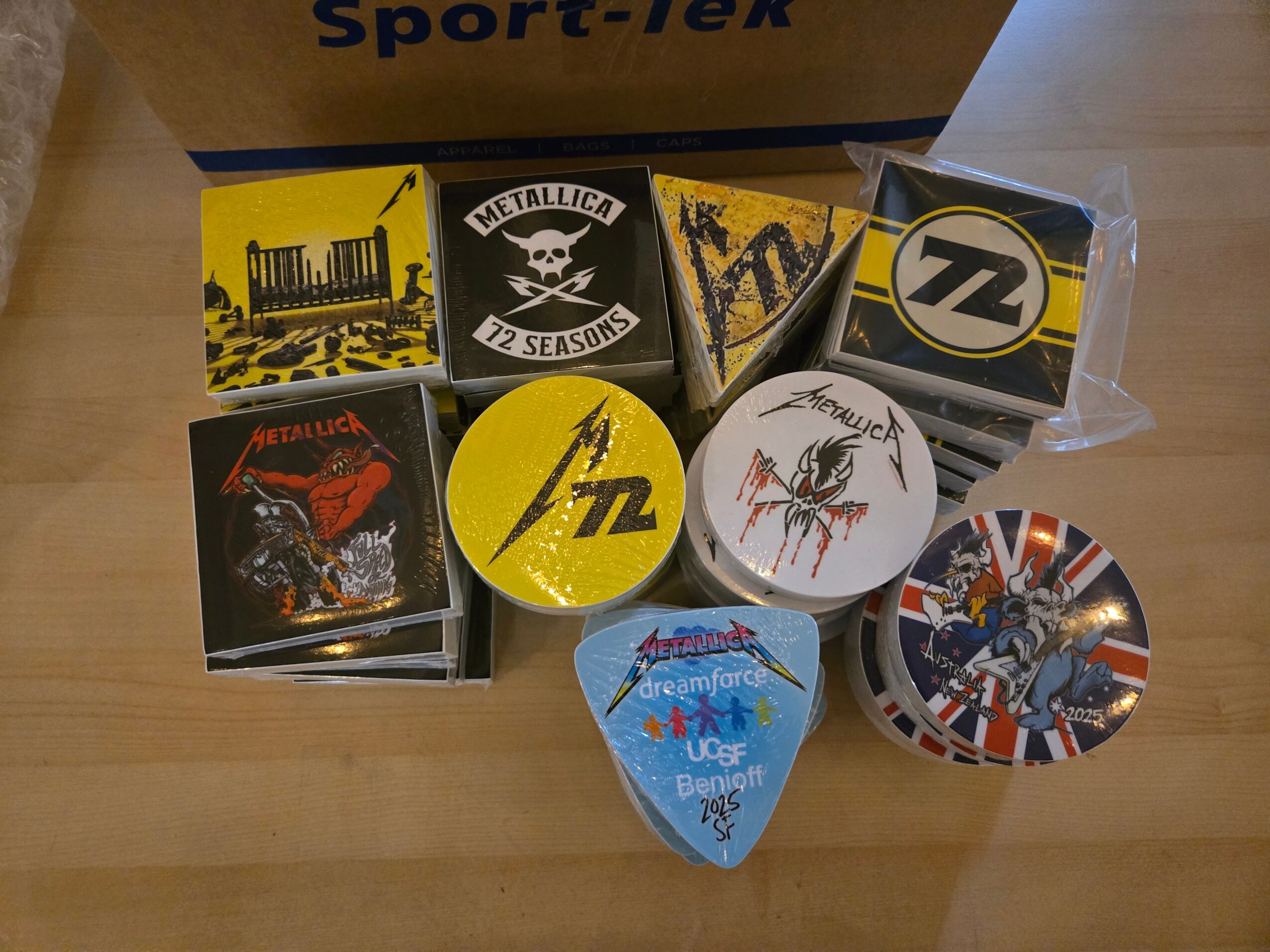 Collection of nine guitar picks with various band logos and designs, arranged on a wooden surface.