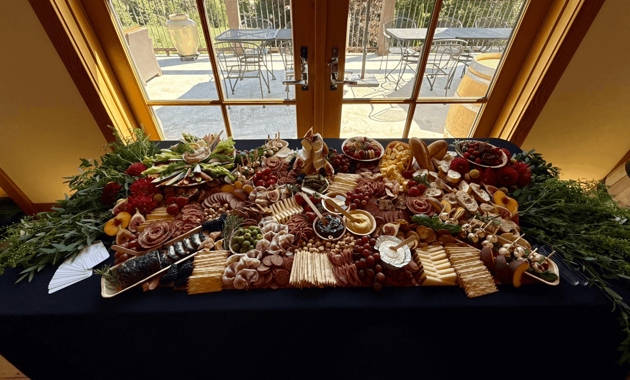 Assorted cheeses, fruits, and snacks on a table near glass doors, with outdoor patio visible outside.