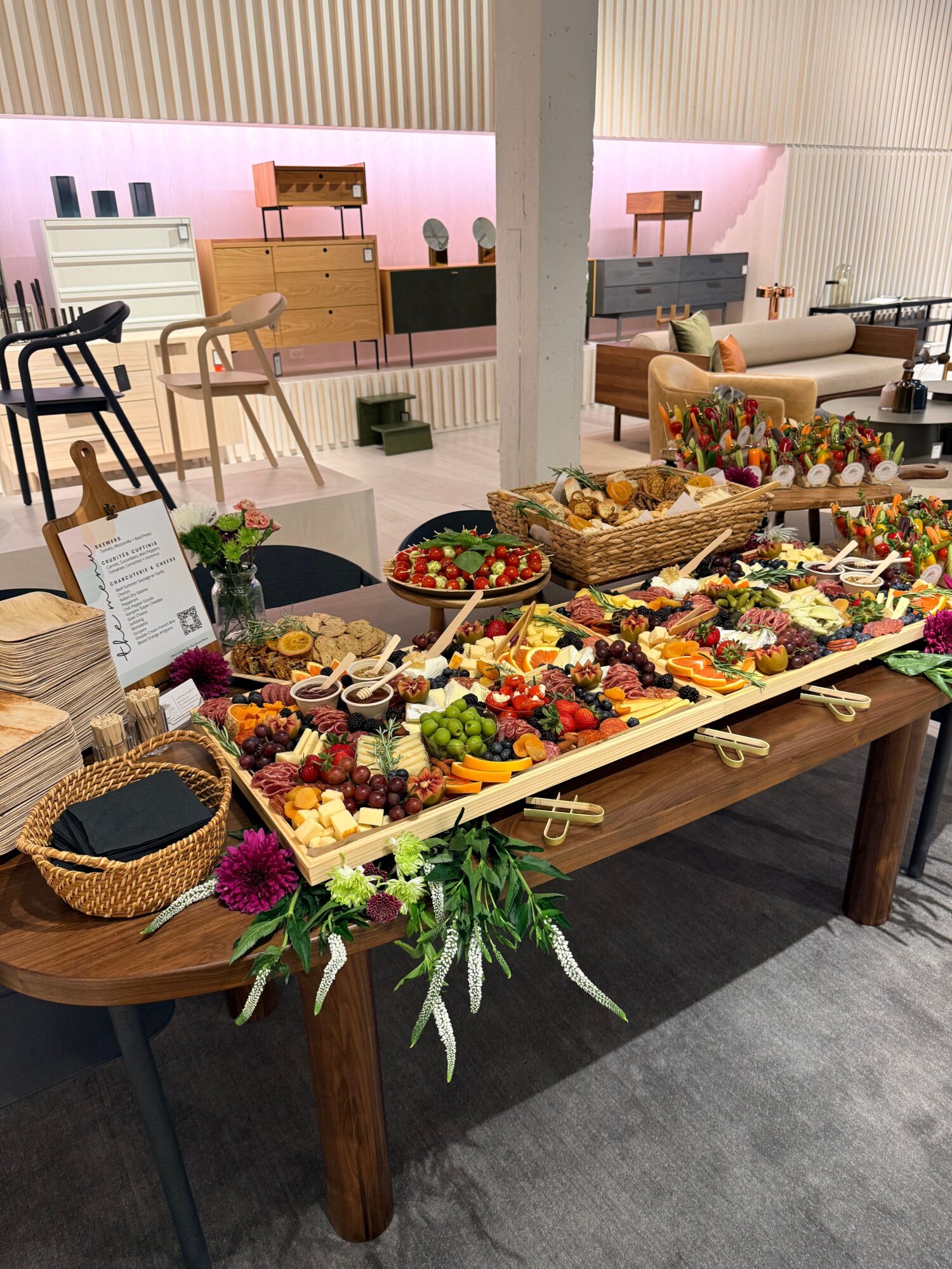 Long table with colorful food and floral decorations in a room with pink and white walls.