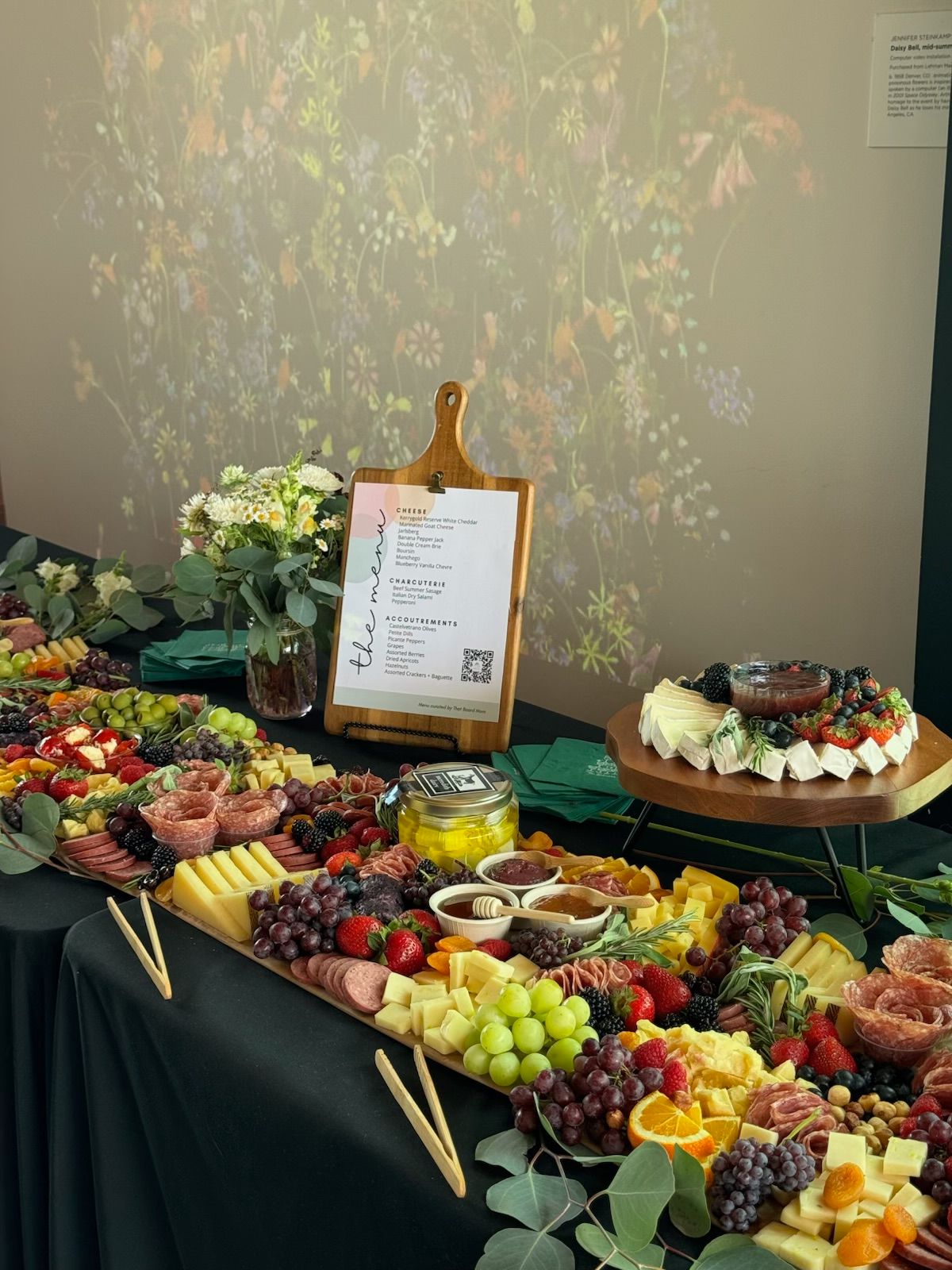 Table with various fruits, flowers, and a cake, with a menu and decorative items, viewed sideways.
