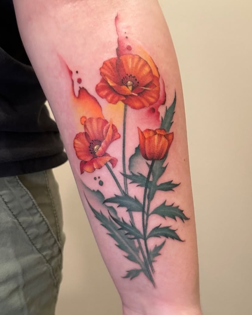 Colorful poppy flower tattoo with green leaves on person's forearm.