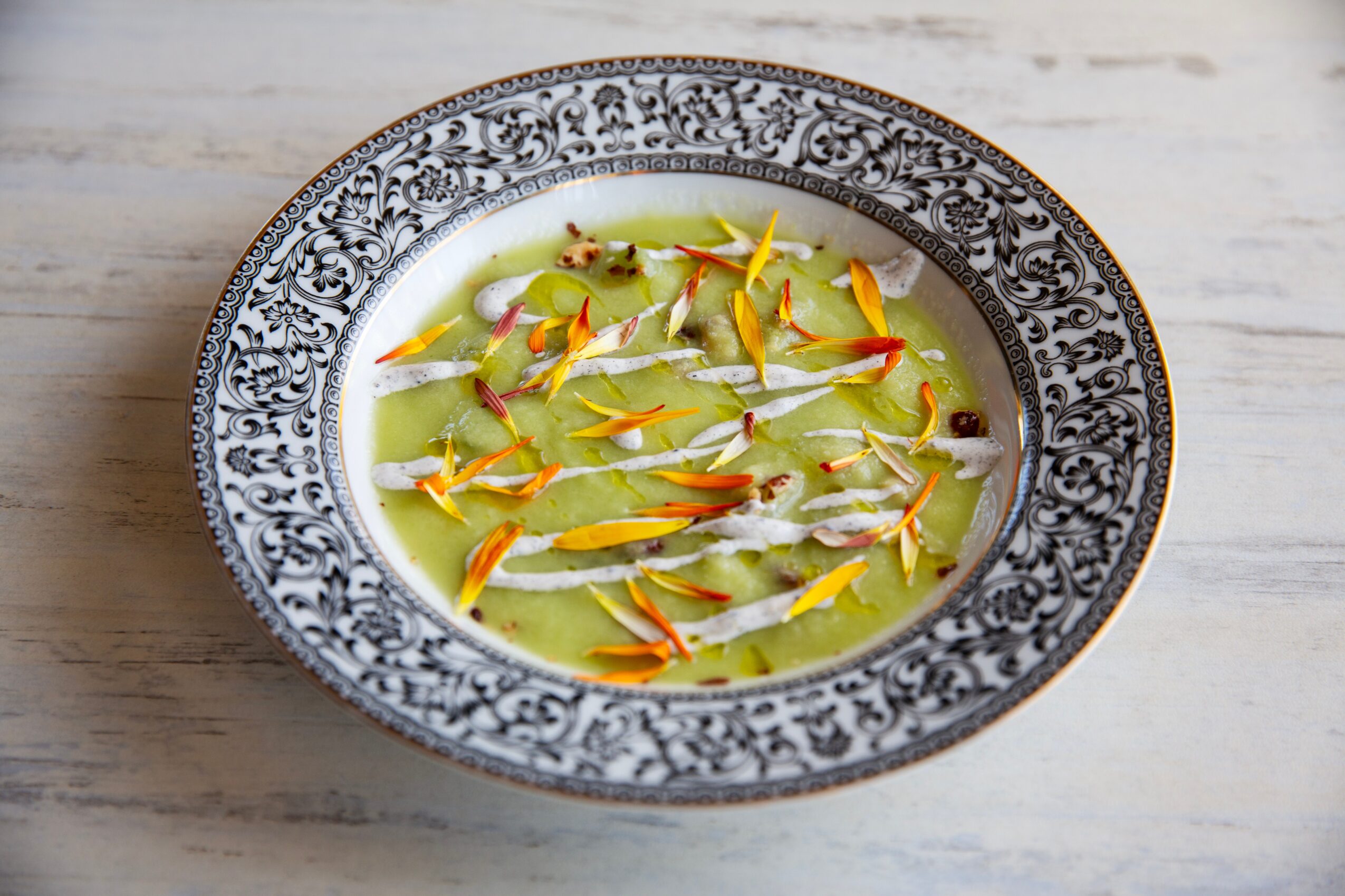 Bowl with yellow and red flower petals floating in a light green liquid, on a light wooden surface.