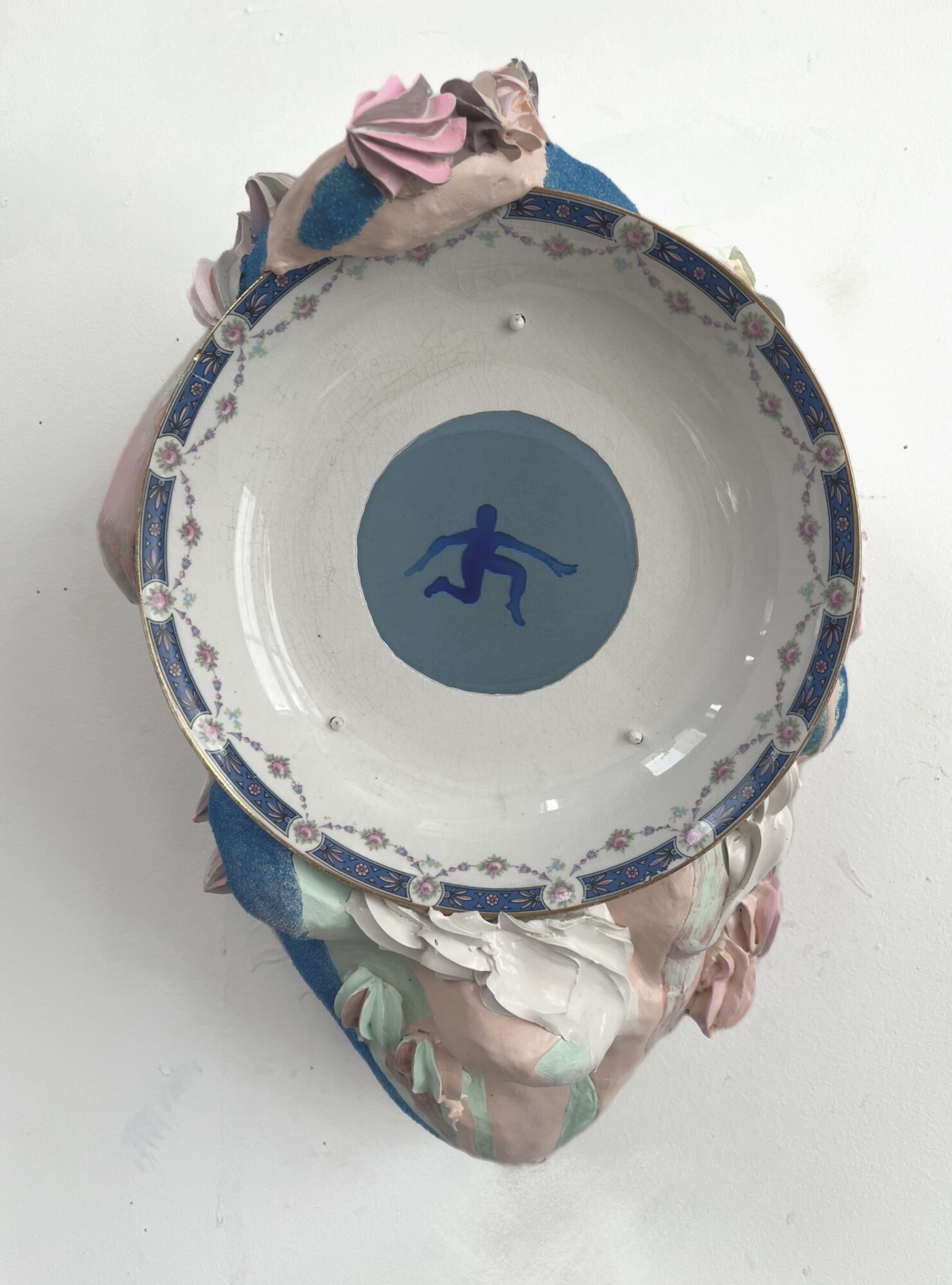 Decorative plate with a blue circle and a silhouette of a person running, placed on a colorful cloth, against a white background.