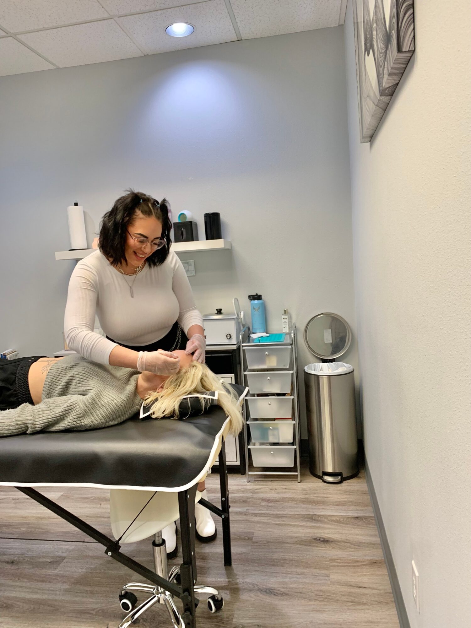 Woman with dark hair and glasses examines a dog on a table in a veterinary clinic room.