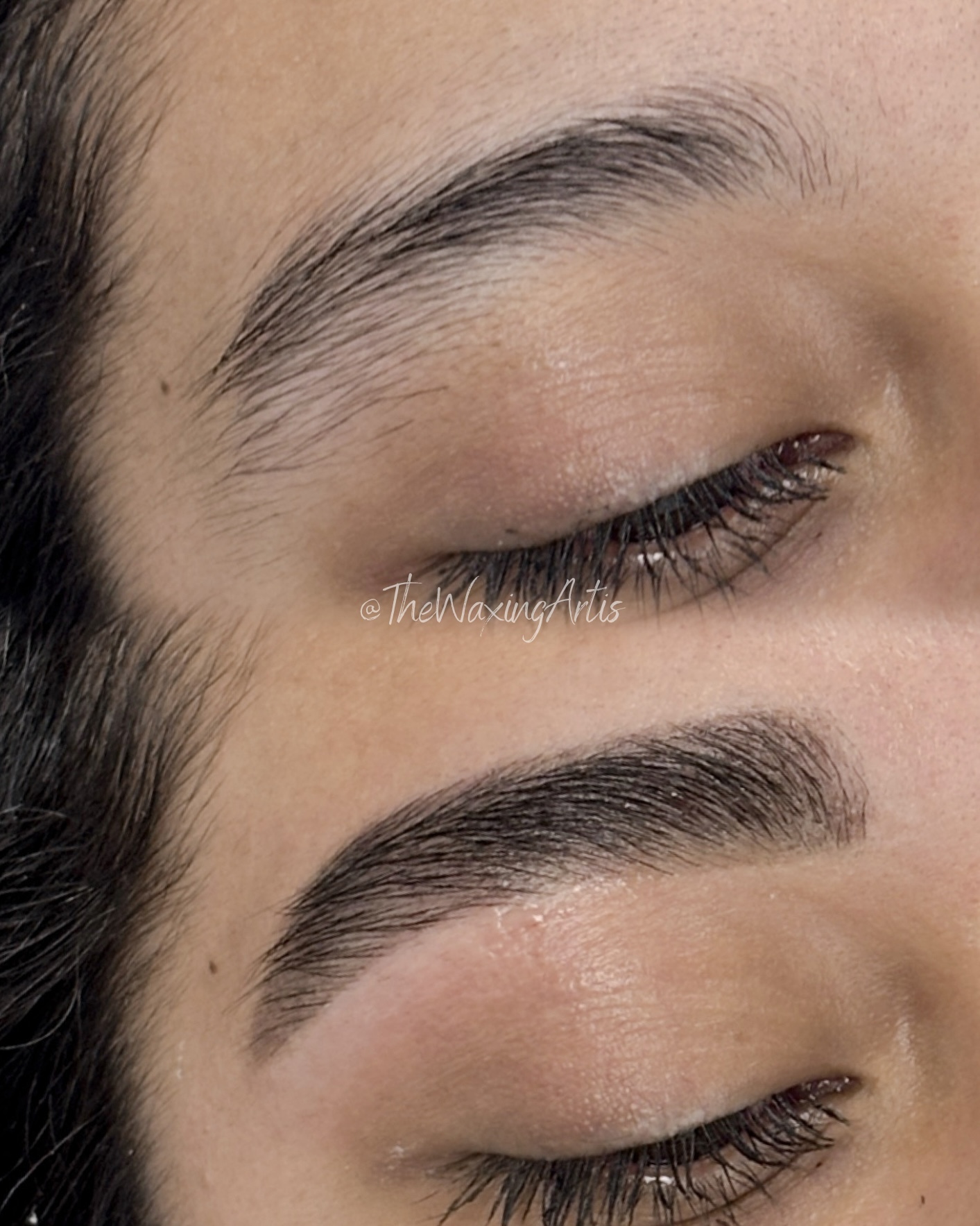 Close-up of a person's closed eye showing well-groomed eyebrows and smooth skin.