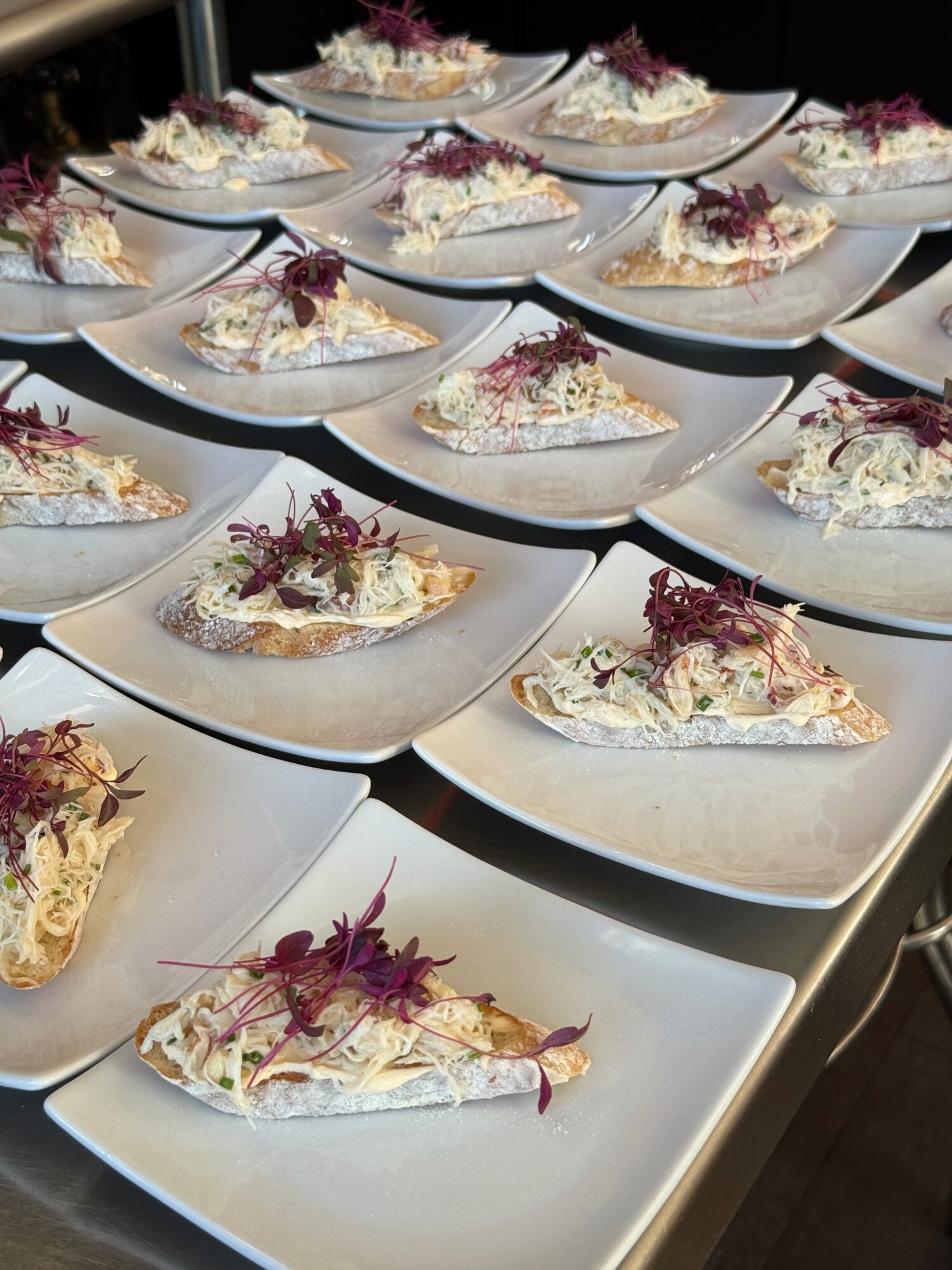 Multiple plates with slices of cake topped with purple and white garnishes, arranged on a white table.