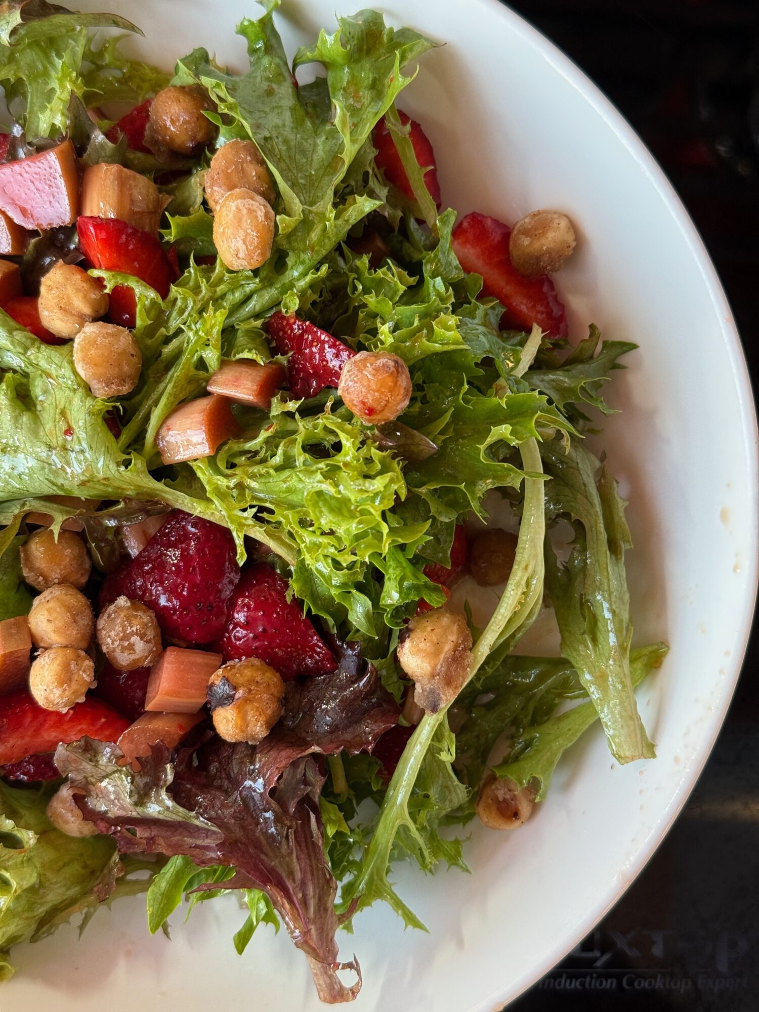 Mixed salad with leafy greens, strawberries, nuts, and chickpeas in a white bowl
