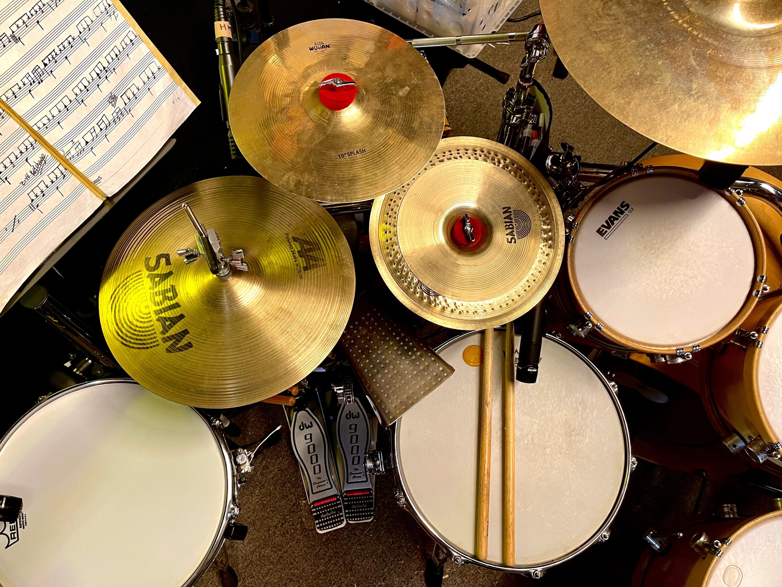 Top view of a drum set with cymbals, drumsticks, and a music sheet, arranged on a stand.