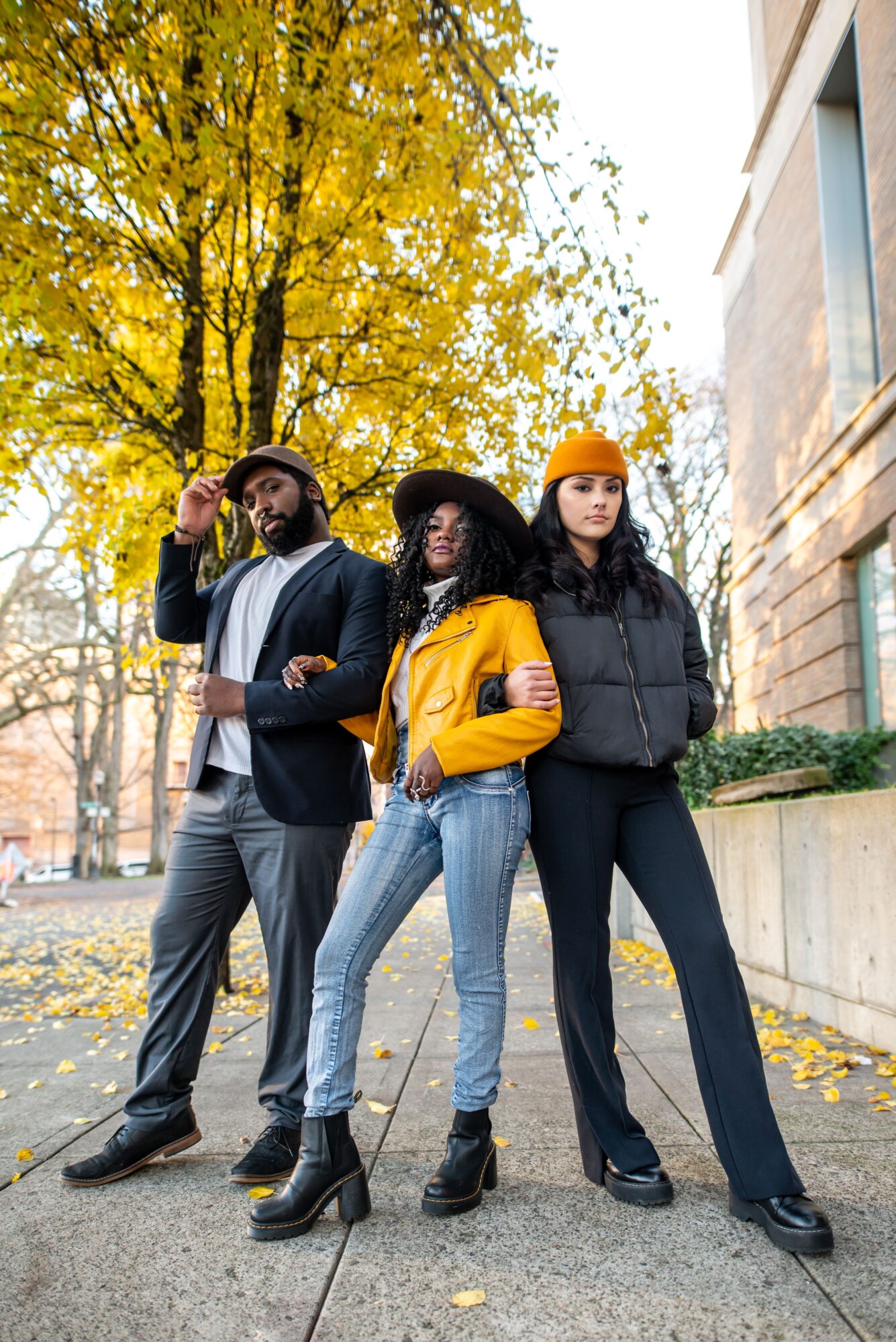 Three people standing outdoors on a sidewalk with autumn trees and buildings in the background.
