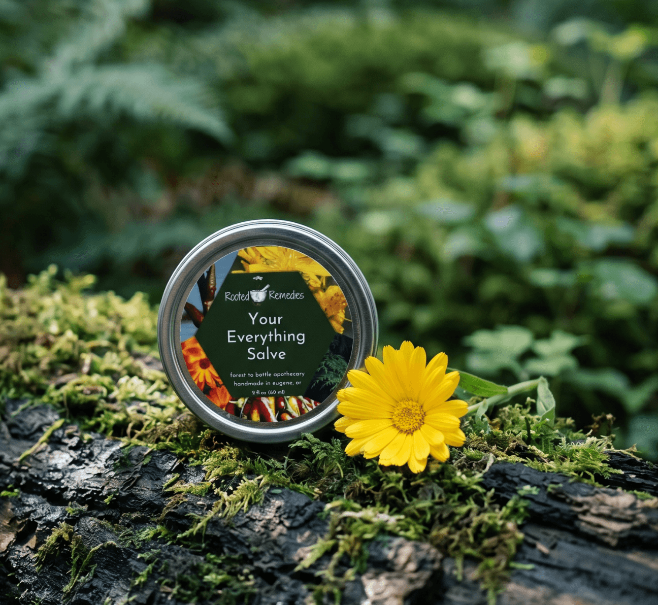 A small container with a label reading 'Your Everything Salve' is placed on a mossy log next to a yellow flower in a green outdoor setting.