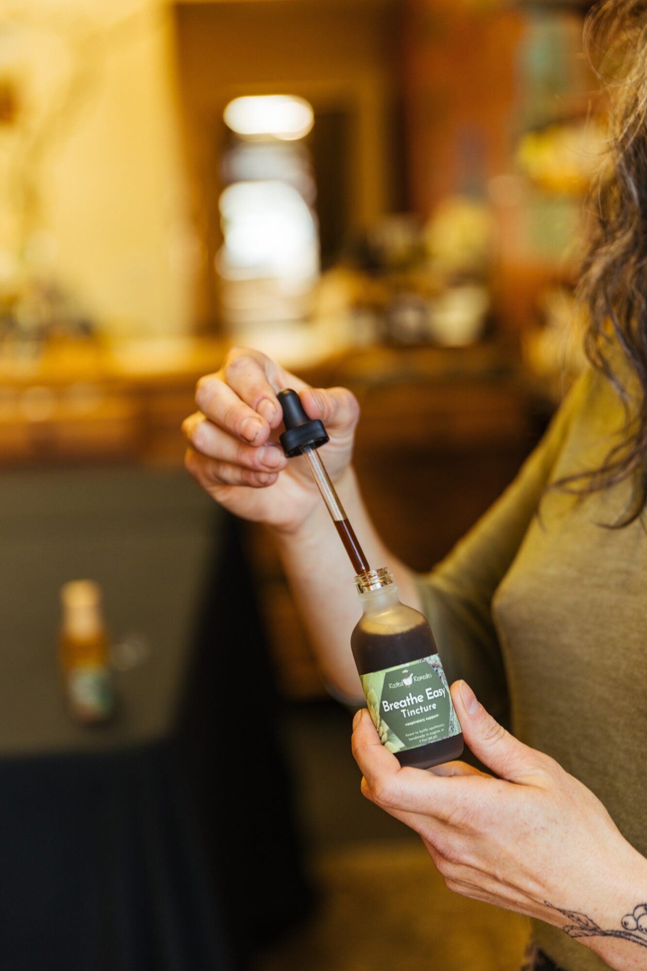 Person holding a small bottle with a dropper, in a warmly lit room with blurred background.