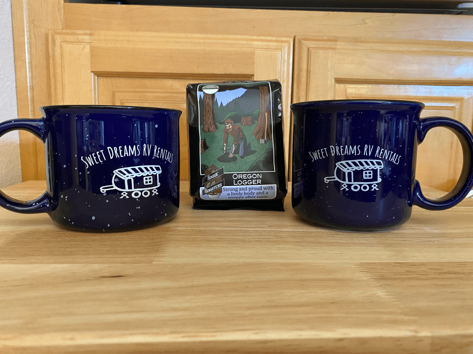 Two dark blue mugs with white text and a small box with a horse image between them on a wooden surface.