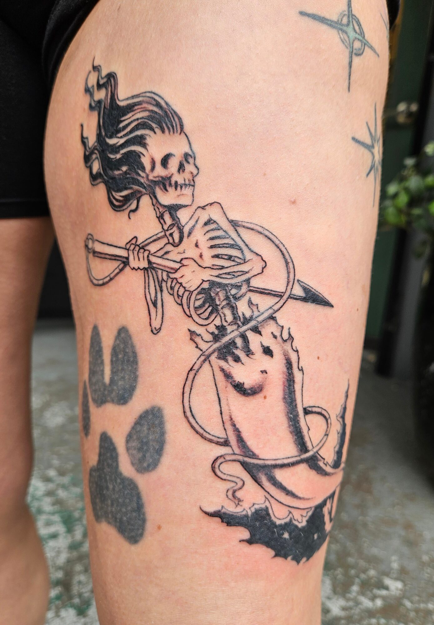 Tattoo of a skeleton with a bow and arrow, surrounded by paw prints and a bat silhouette, on a person's arm.