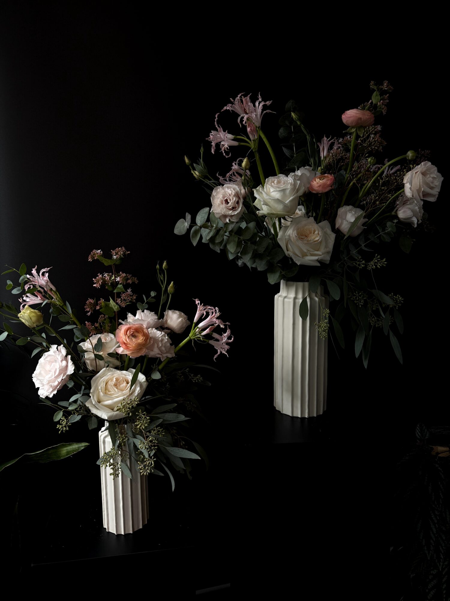 Two floral arrangements in striped vases with pink and white flowers against a dark background.