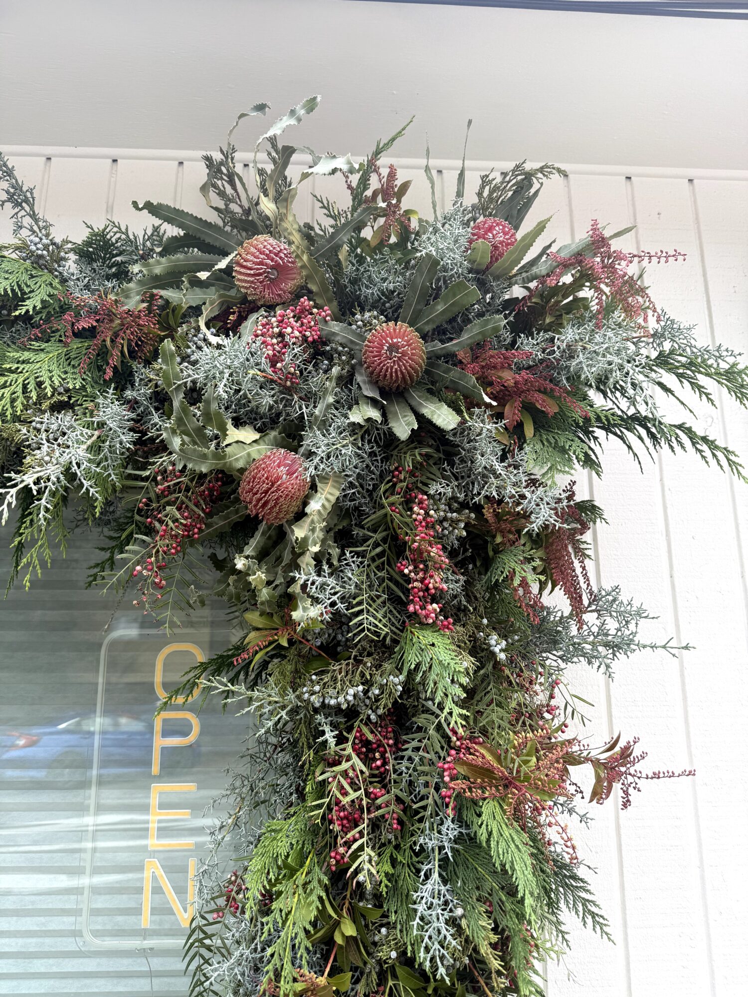 A large floral arrangement with various green, pink, and red plants and flowers, hanging on a white wall.