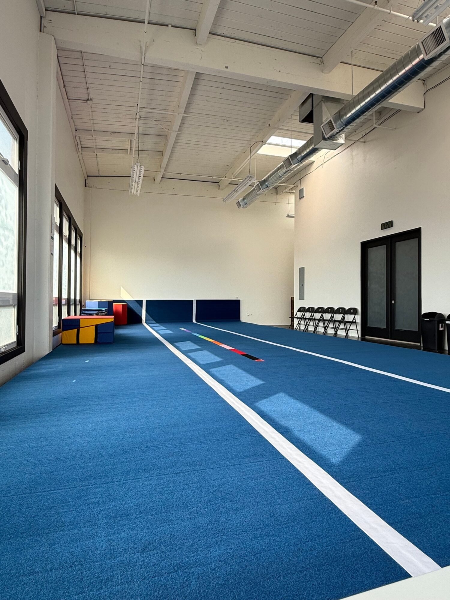 Indoor gym with blue mat, white lines, and equipment along the wall, viewed from the side.