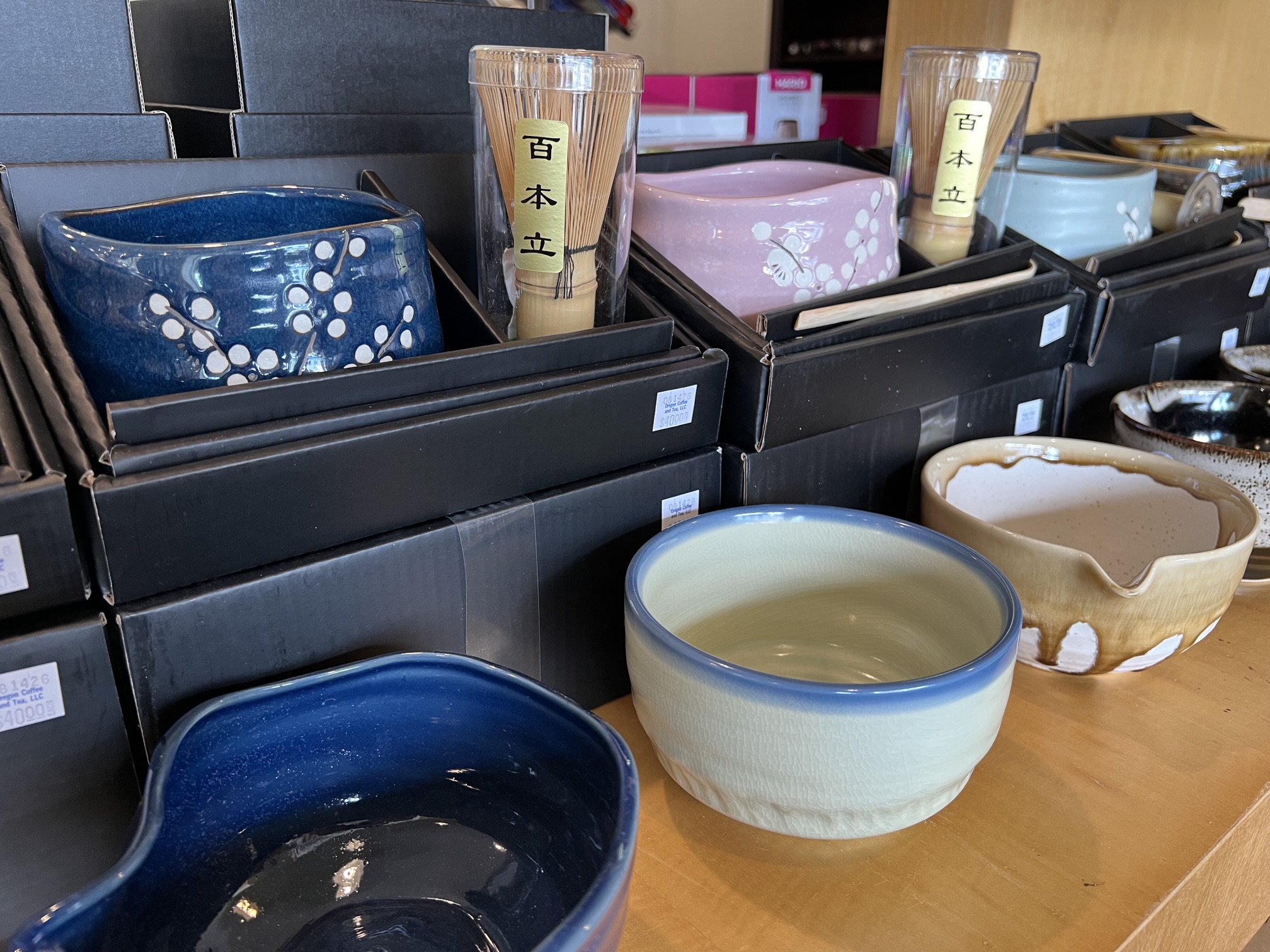 Various ceramic bowls and cups on a wooden surface with boxes and containers in the background.