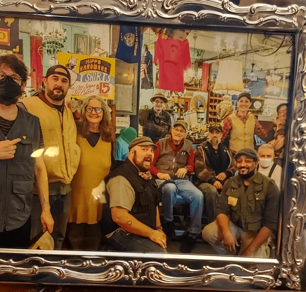 Group of people in a store, some wearing masks, posing for a photo, with shelves and clothing in the background.