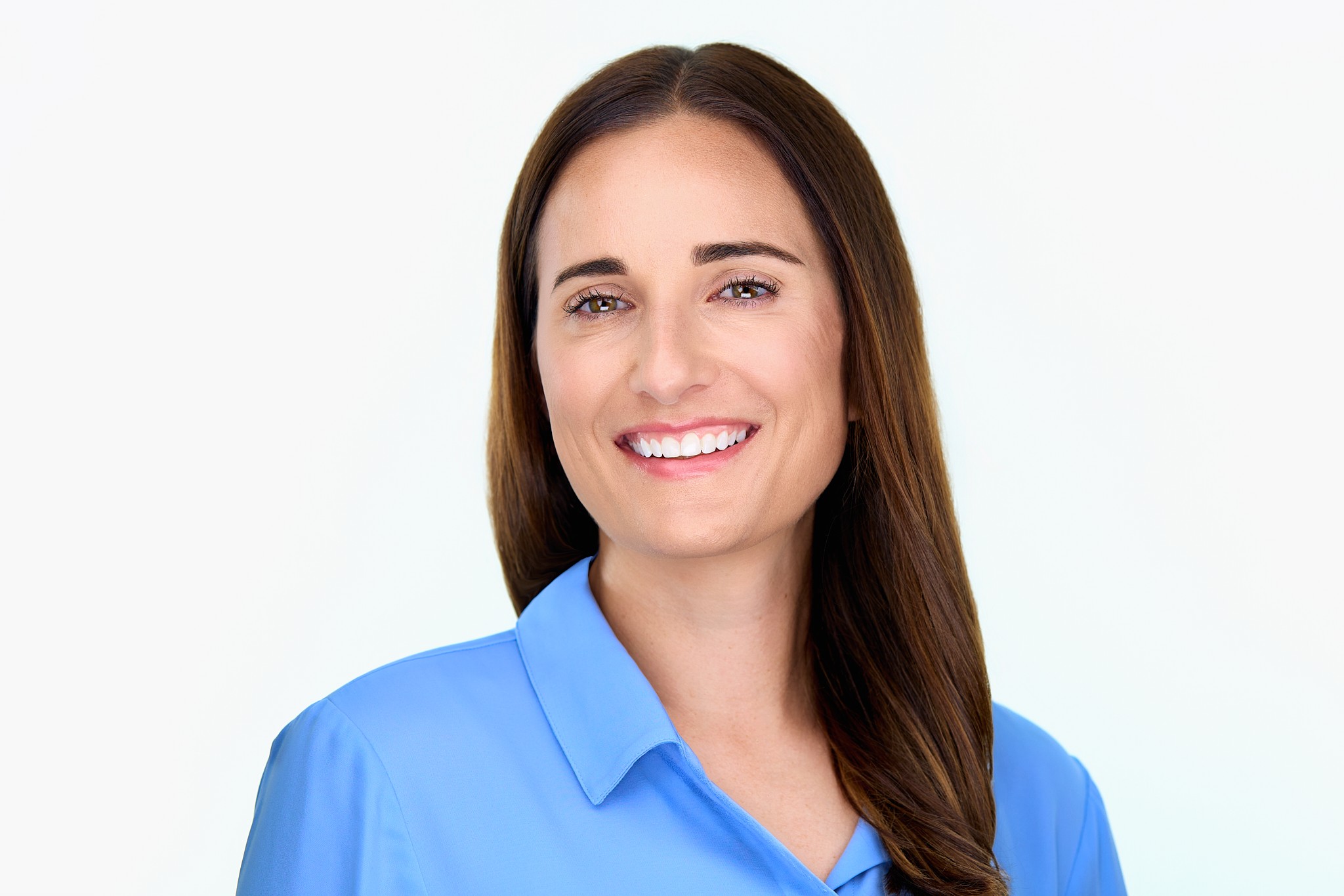 Smiling woman with long brown hair wearing a blue shirt against a white background.