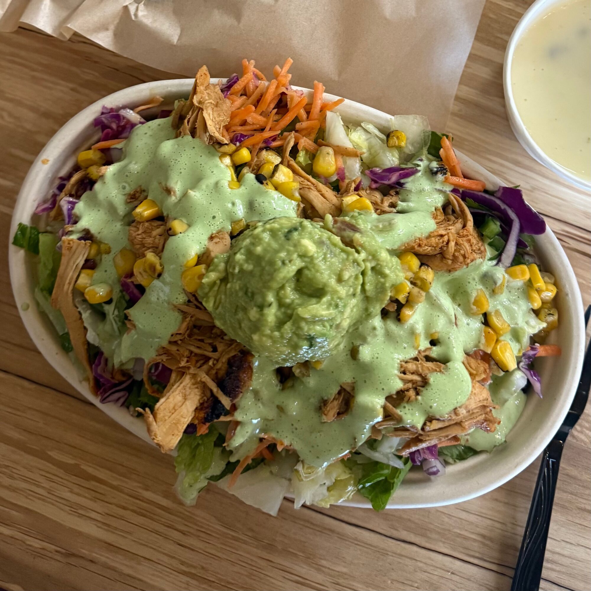 Salad with shredded chicken, corn, carrots, lettuce, purple cabbage, topped with green dressing and guacamole, on a white dish.